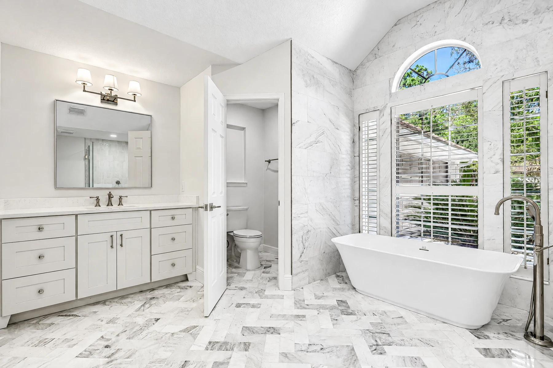 White recessed-panel bathroom vanity with a central double-door cabinet and drawer stacks beside a freestanding tub.