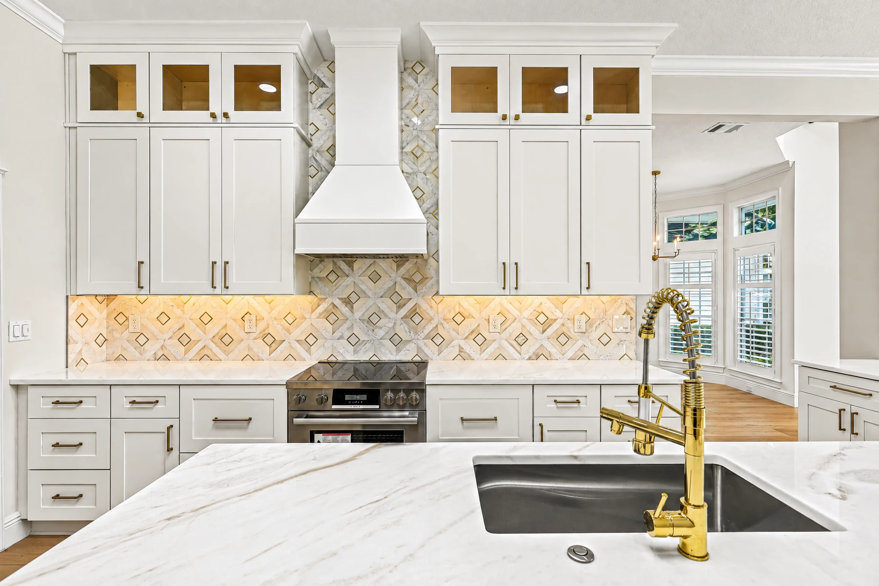 White kitchen range-wall cabinetry with glass-front upper cabinets and warm metal hardware.