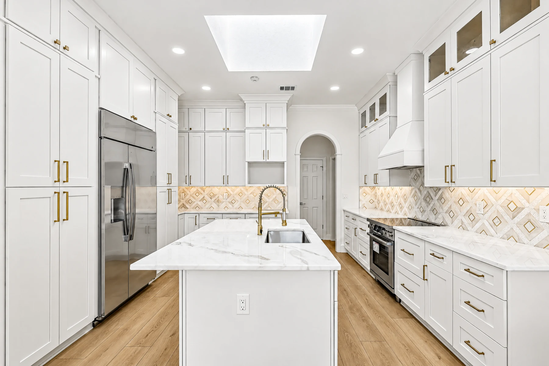 White recessed-panel kitchen cabinets with glass-front uppers, tall storage and a central island.
